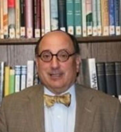 Professor Stravitz with round glasses and a bow tie, with library bookshelves behind him